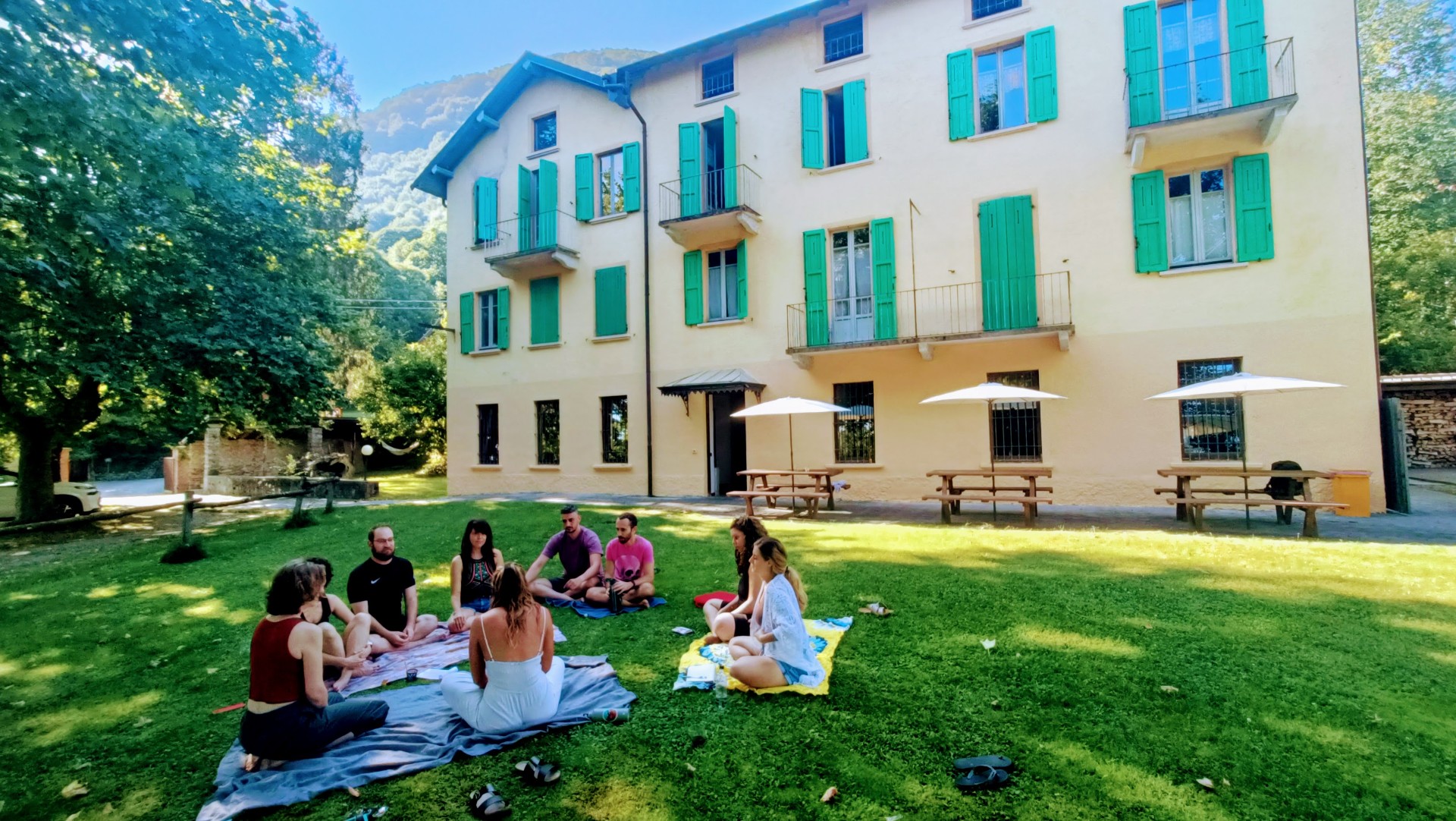Remote workers sitting together on the lawn in front of the Montino Coliving house near Lago Maggiore, Italy